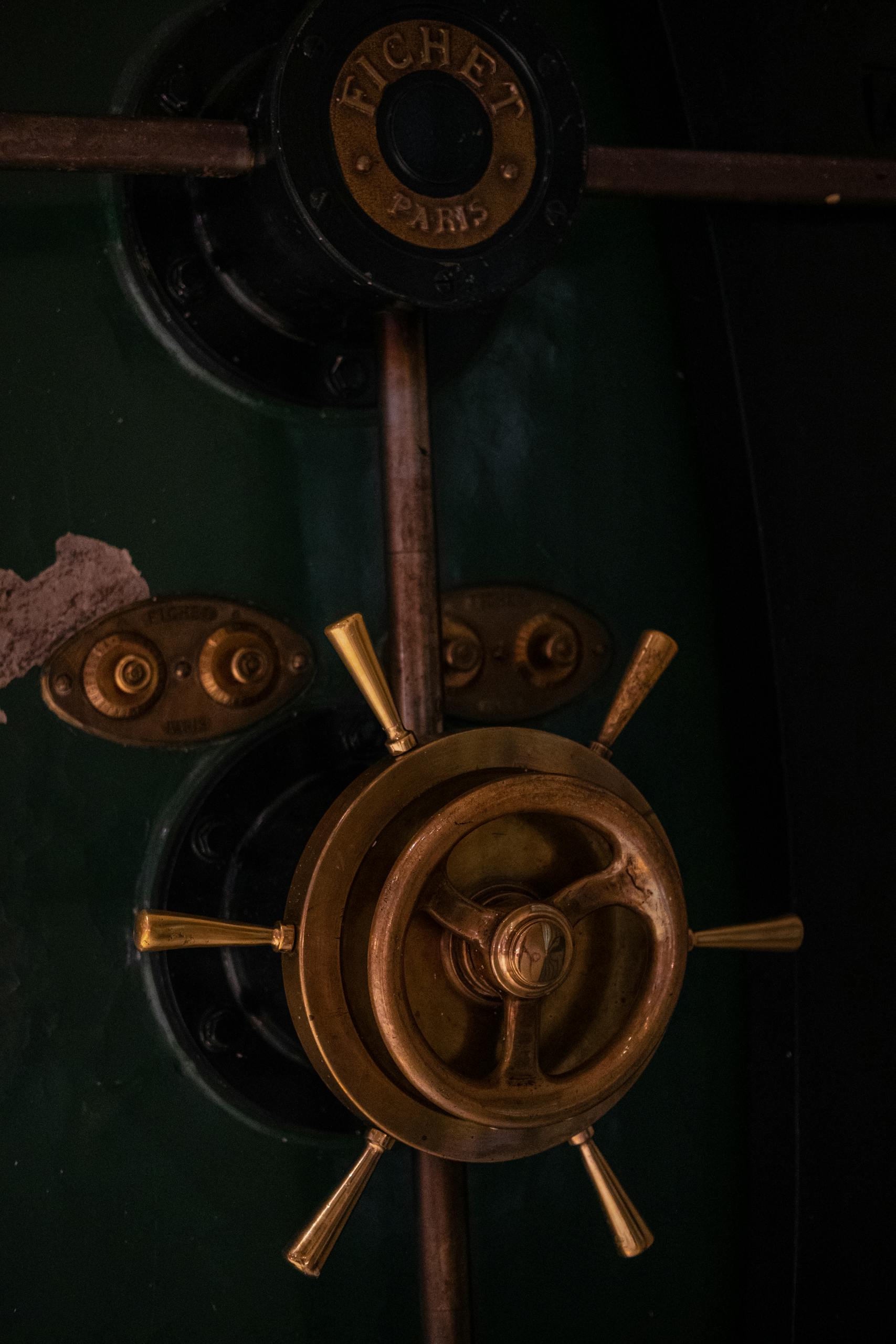 Close-up of a vintage safe door with a brass handle and dark green surface.